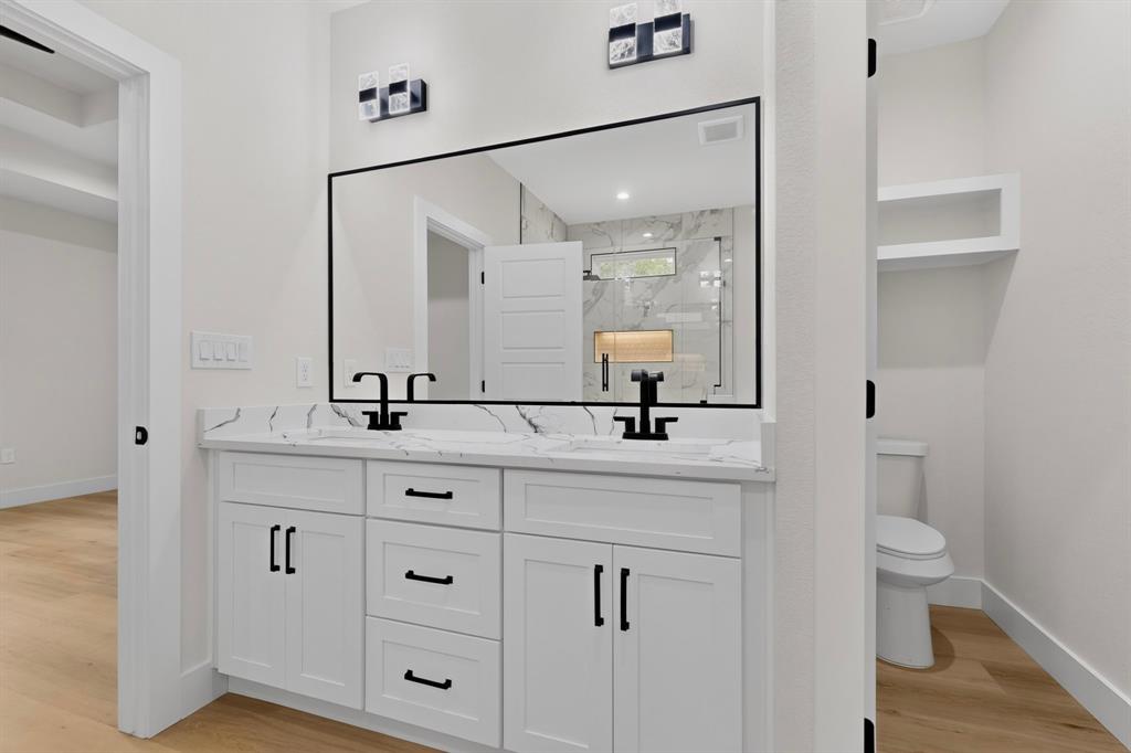 Dual vanity with white cabinetry and black hardware, stone-finish countertop, and integrated sinks