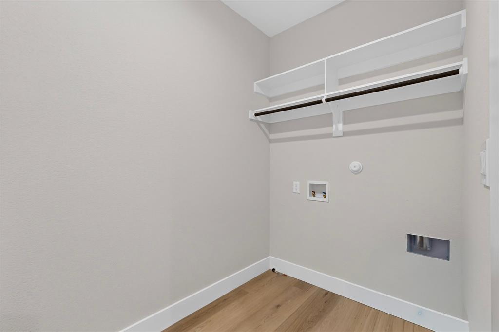 Dedicated laundry area featuring wood-finish flooring, white trim, and built-in shelving with hanging rods
