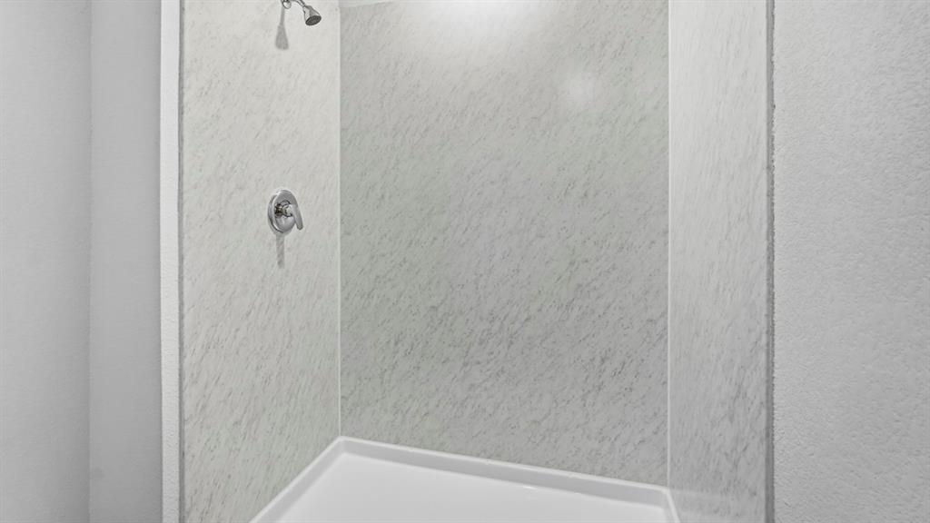 Enclosed shower with a white acrylic base and textured wall panels, featuring a chrome shower head and control handle