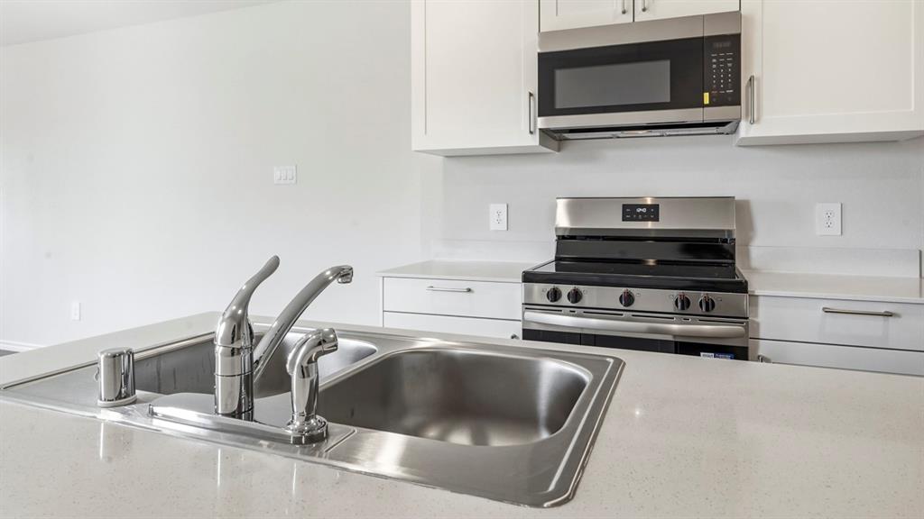 Stainless steel double basin sink with chrome faucet, white cabinetry, integrated stainless steel microwave, and stainless steel range Stainless steel double basin sink with chrome faucet, white cabinetry, integrated stainless steel microwave, and stainless steel range