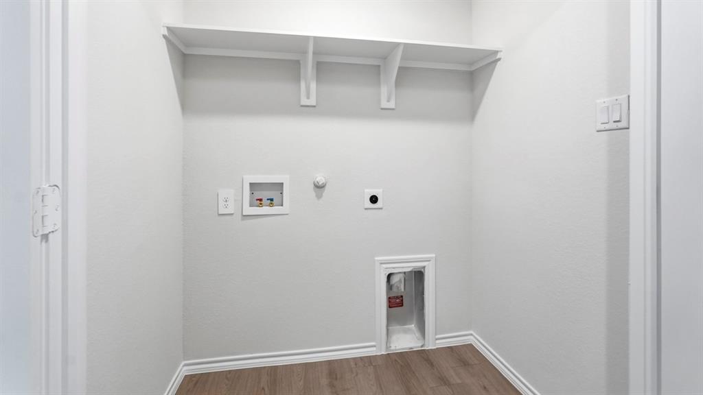 Utility space featuring wood-finish flooring, built-in shelving, and white baseboards Utility space featuring wood-finish flooring, built-in shelving, and white baseboards