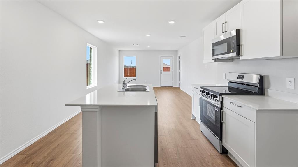 Kitchen featuring an island with a stainless steel sink, white cabinetry, stainless steel appliances, and wood-finish flooring Kitchen featuring an island with a stainless steel sink, white cabinetry, stainless steel appliances, and wood-finish flooring