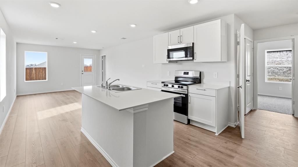Kitchen island with an undermount dual-basin sink, stainless steel appliances, white cabinetry, and wood-finish flooring throughout Kitchen island with an undermount dual-basin sink, stainless steel appliances, white cabinetry, and wood-finish flooring throughout
