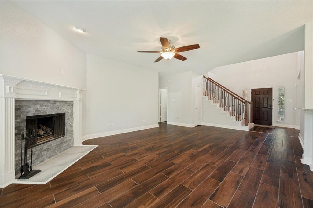 Vaulted ceiling with a ceiling fan, wood-finish flooring, fireplace with stone surround and mantle, and a staircase with wood and metal railing