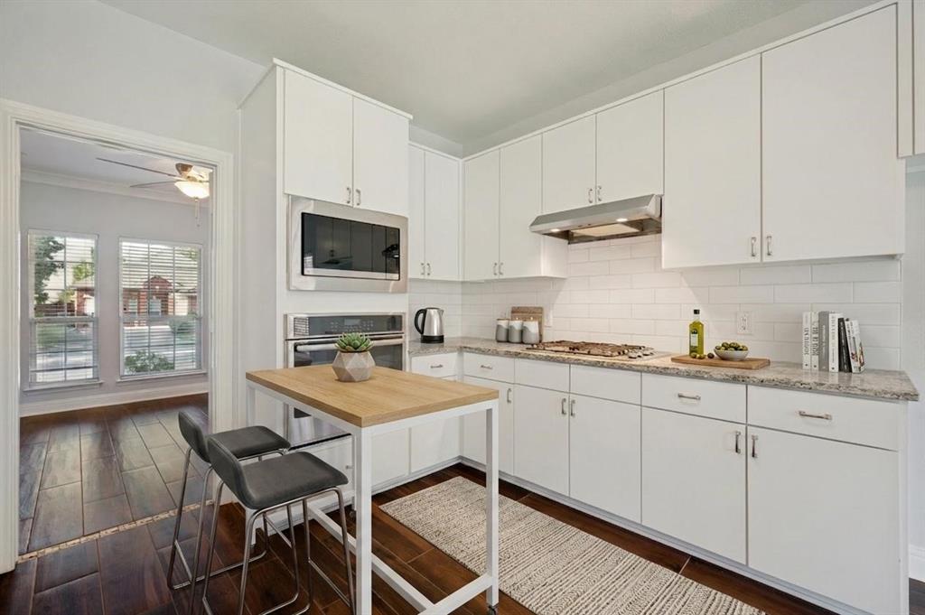 White cabinetry, integrated stainless steel appliances, subway tile backsplash, light-toned countertop, and wood-finish flooring