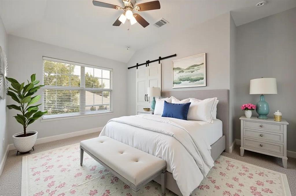 Vaulted ceiling with a ceiling fan, dual windows with blinds, and a barn door leading to an interior space