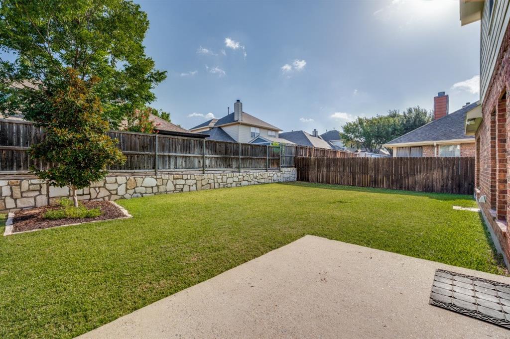 Expansive green lawn, brick exterior, concrete patio, privacy fencing, and stone retaining wall