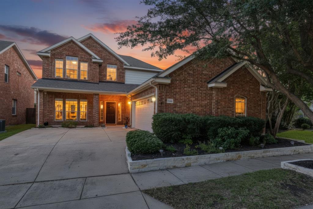 Brick exterior with white trim, multi-pane windows, attached garage, concrete driveway, and landscaped front beds