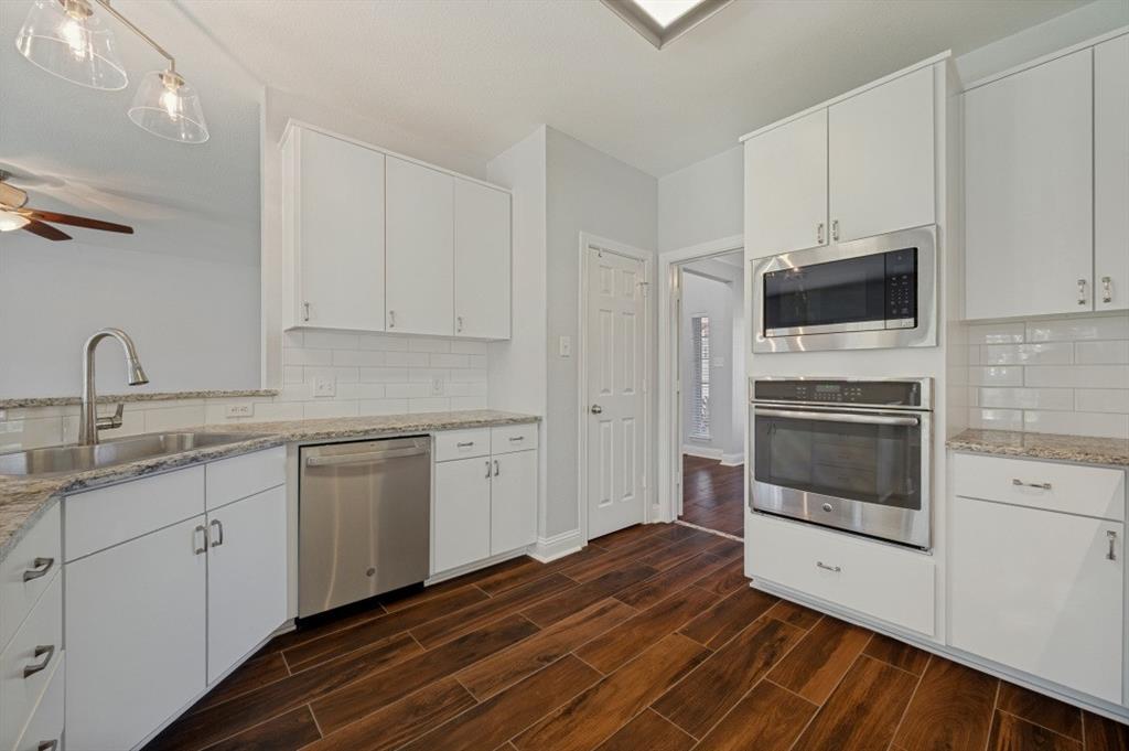 Kitchen featuring white cabinetry, stainless steel appliances, speckled stone countertops, a subway tile backsplash, and wood-finish flooring