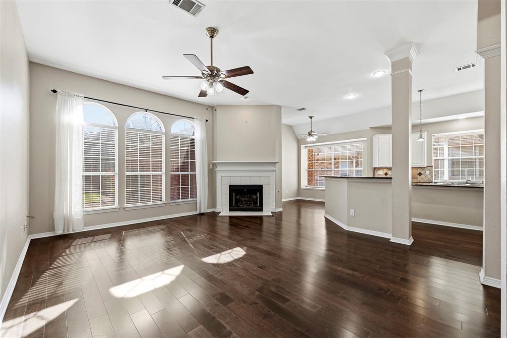 Spacious living area featuring wood-finish flooring, a fireplace with a white mantel, and arched windows