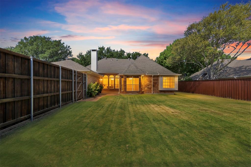 Expansive backyard featuring a manicured lawn, a full-height privacy fence, and a brick exterior with multiple windows