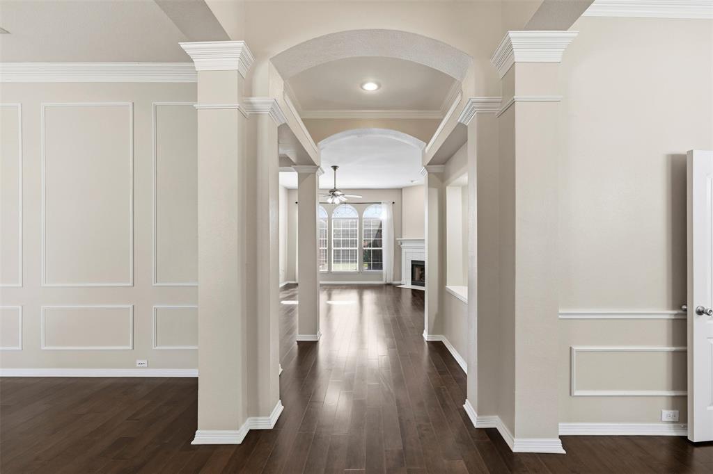Arched entryway with substantial columns, dark wood-finish flooring, and decorative wall paneling Arched entryway with substantial columns, dark wood-finish flooring, and decorative wall paneling
