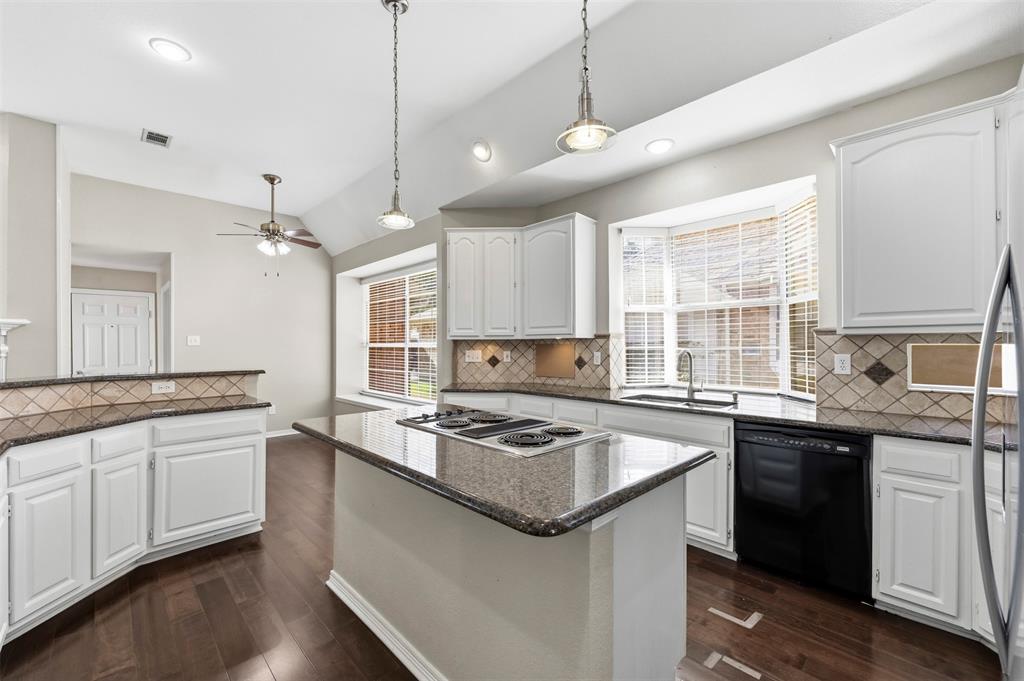 Kitchen featuring white cabinetry, dark wood-finish flooring, a central island with cooktop, black appliances, and a bay window