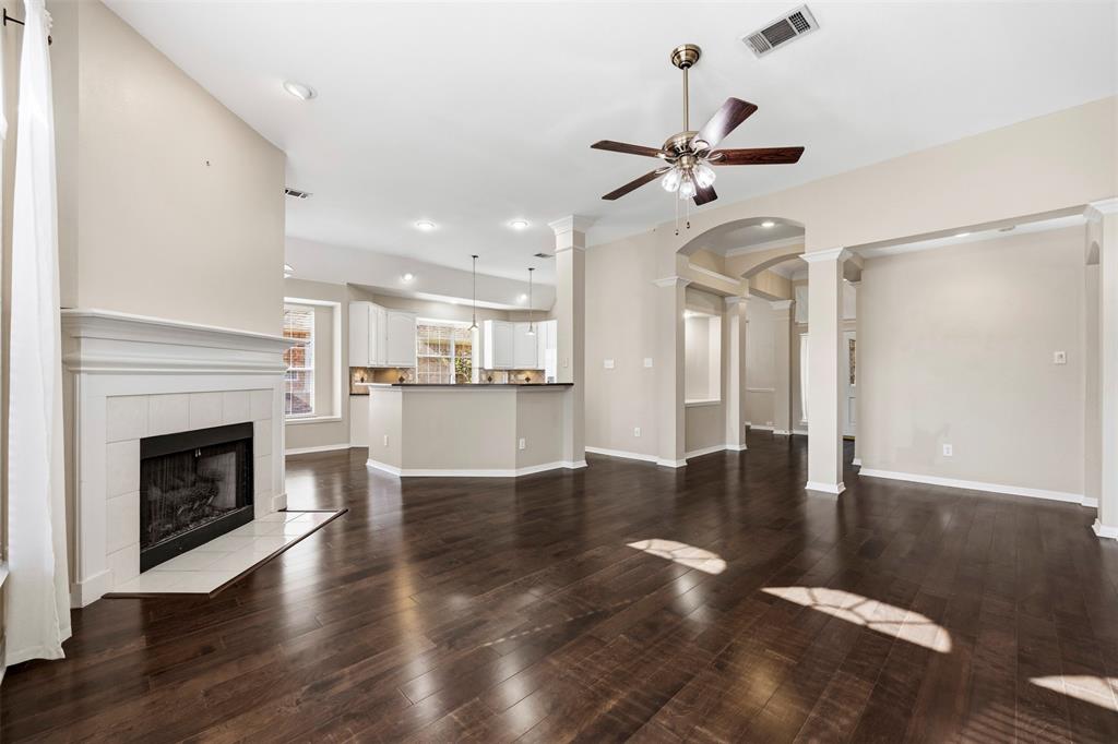 Wood-finish flooring, a white mantel fireplace, and ceiling fan with integrated lighting