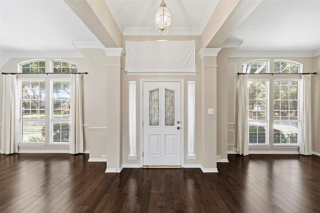 Dark wood-finish flooring, white paneled entry door with decorative glass, arched transom windows, crown molding, and a decorative pendant light fixture Dark wood-finish flooring, white paneled entry door with decorative glass, arched transom windows, crown molding, and a decorative pendant light fixture