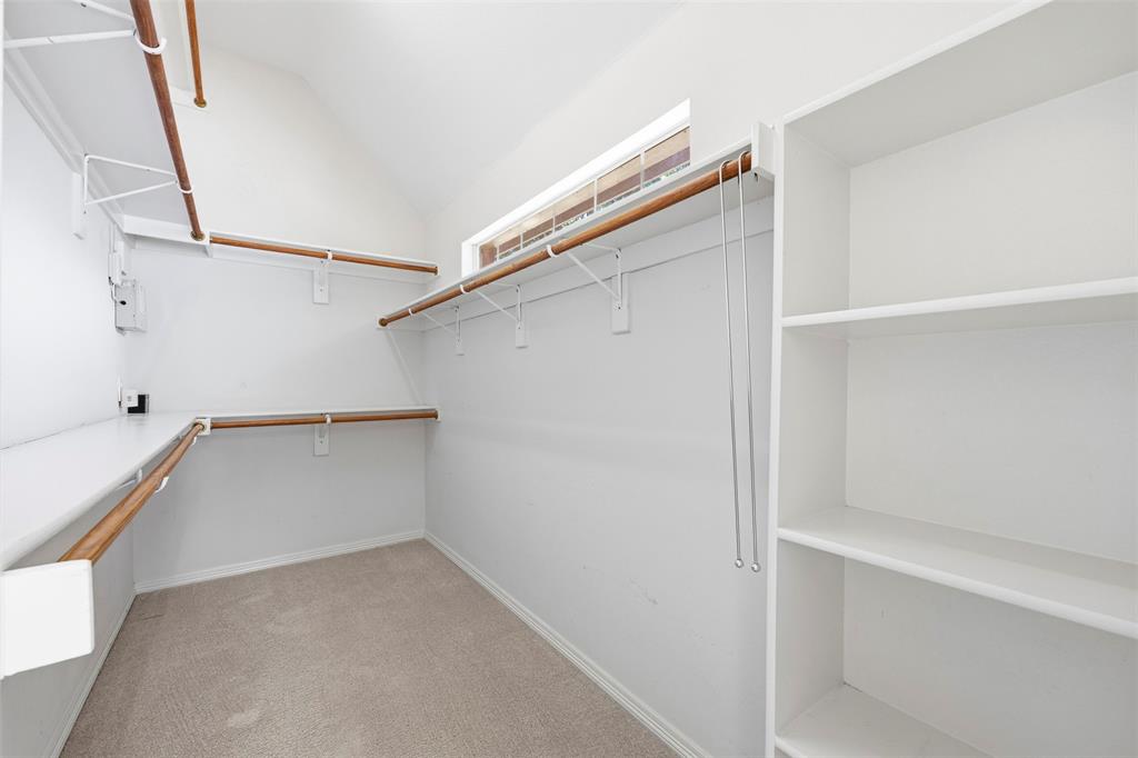 Expansive closet featuring integrated shelving, multiple wood-finish hanging rods, and a high window for natural light
