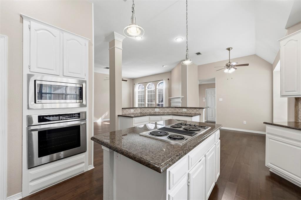 Kitchen featuring an island with a built-in cooktop, white cabinetry, granite countertops, and stainless steel built-in appliances