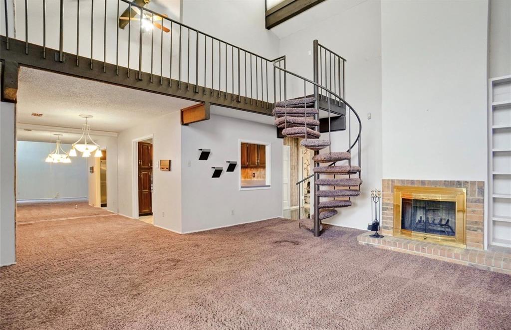 Spiral staircase, brick fireplace with brass surround, built-in shelving, loft area, and vaulted ceilings