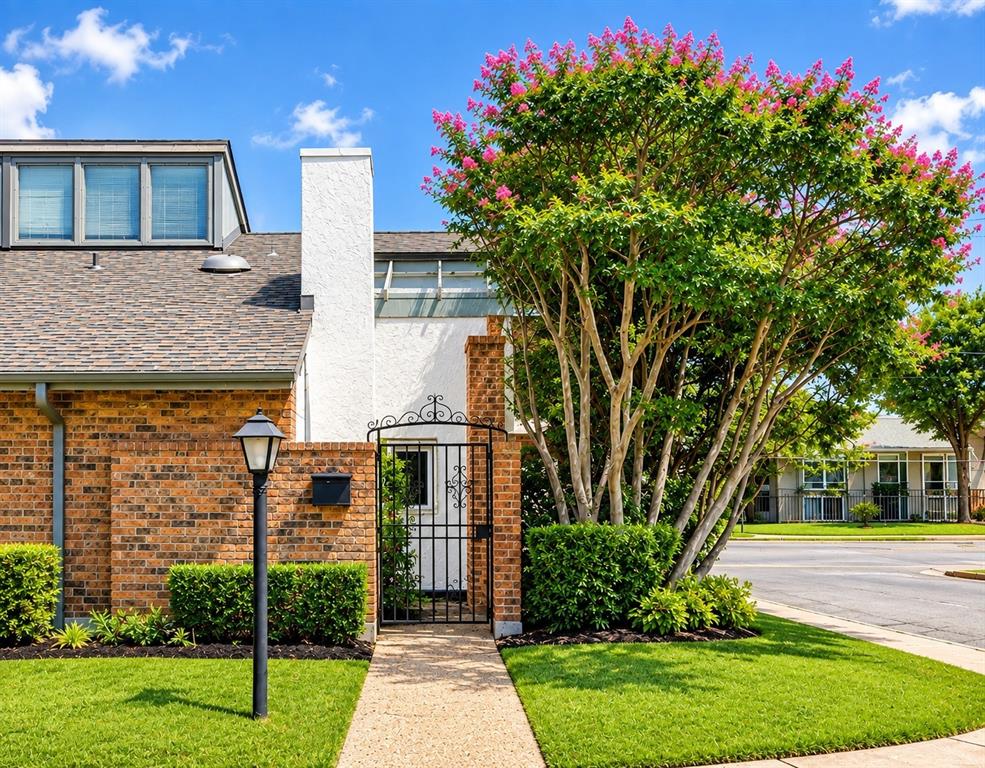 Red brick facade with a white stucco chimney, dormer windows, a wrought iron gate, and a flowering tree