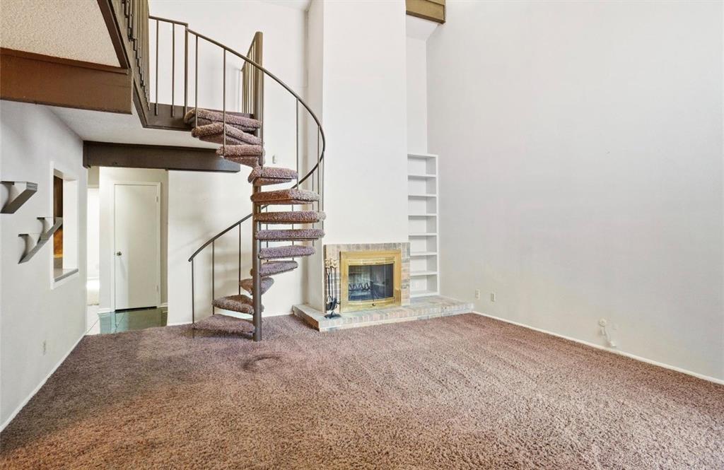 Spacious open floor plan featuring neutral carpet flooring, soaring two-story ceilings, and an architectural spiral staircase with metal railings