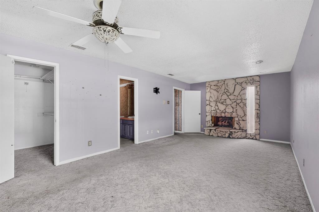 Stone-faced fireplace with a hearth, interior closet with shelving, and a ceiling fan with decorative light fixture