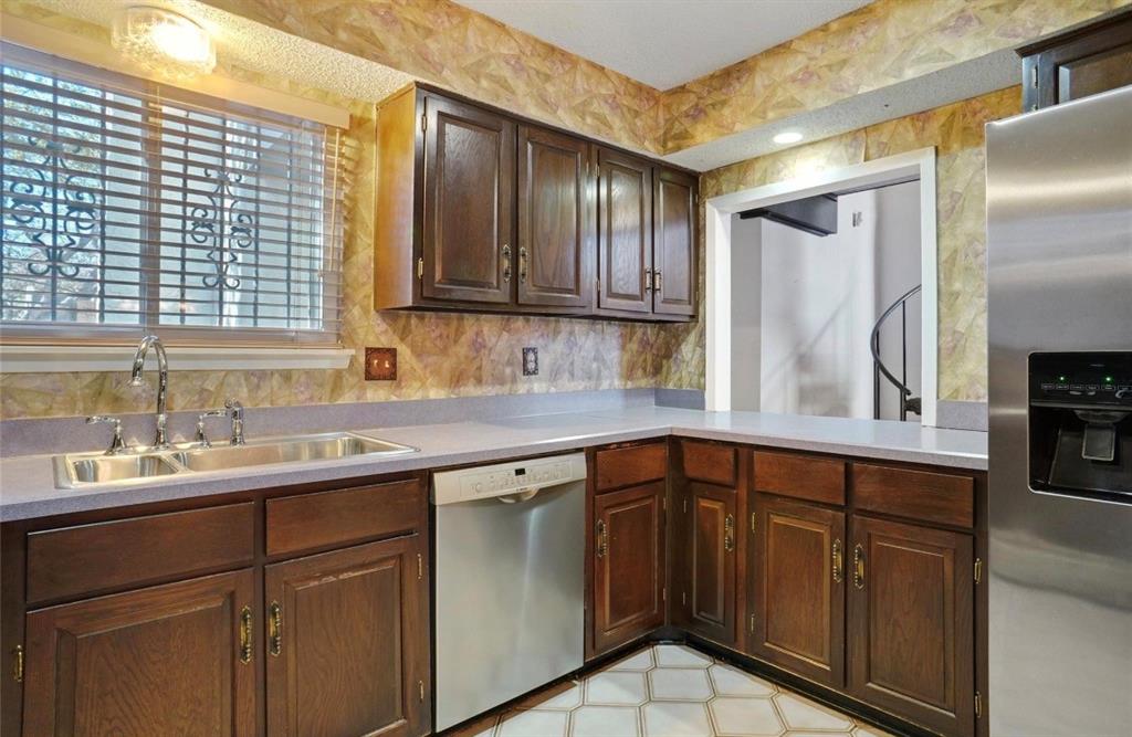 Kitchen featuring wood cabinetry, stainless steel dishwasher, stainless steel refrigerator, dual basin sink, and counter space
