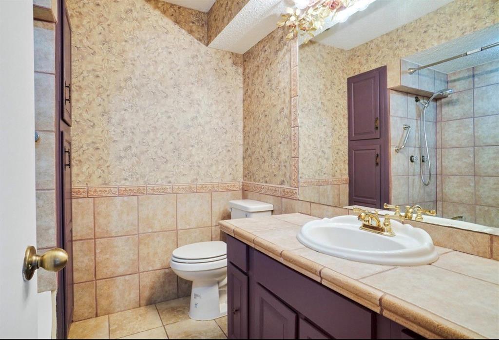 Vanity with an integrated sink and brass-finish faucet, tile countertop, built-in cabinetry, and tile flooring
