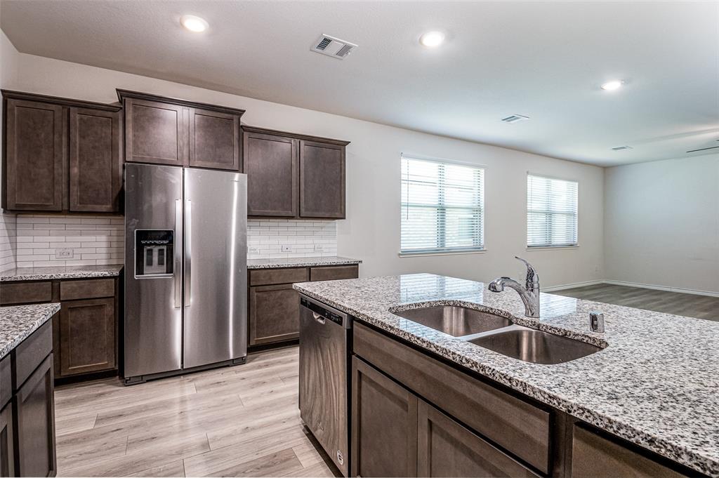 Kitchen featuring dark wood-finish cabinetry, stainless steel appliances, granite countertops, white subway tile backsplash, and wood-finish flooring