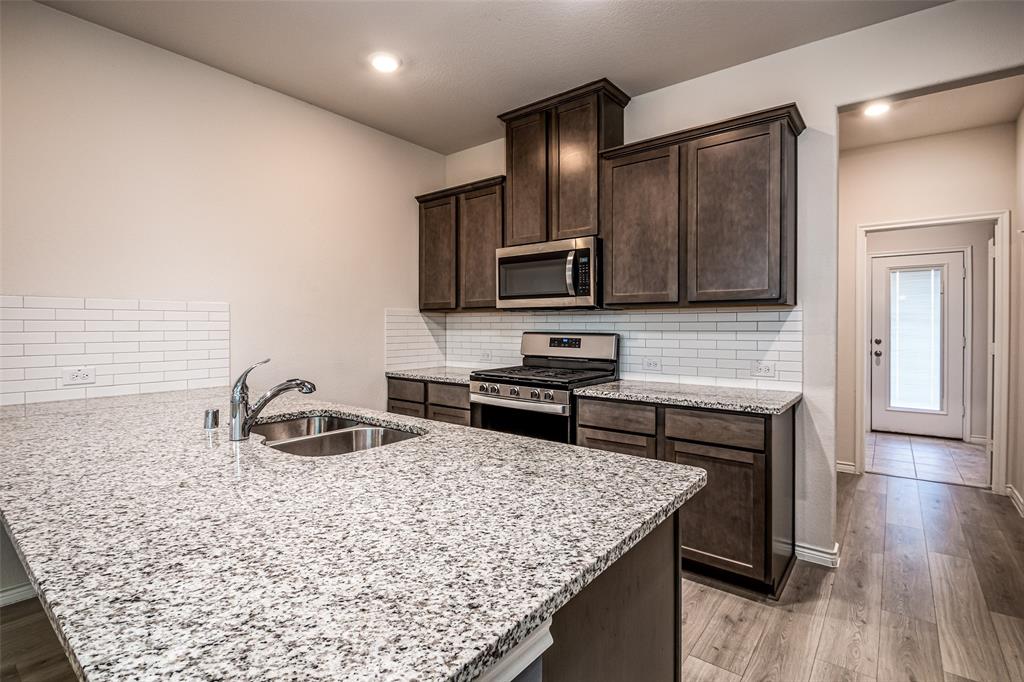 Kitchen featuring granite countertops, stainless steel appliances, dark wood cabinetry, a subway tile backsplash, and wood-finish flooring