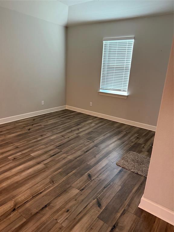 Wood-finish flooring with white trim, light gray wall tones, and a window with blinds