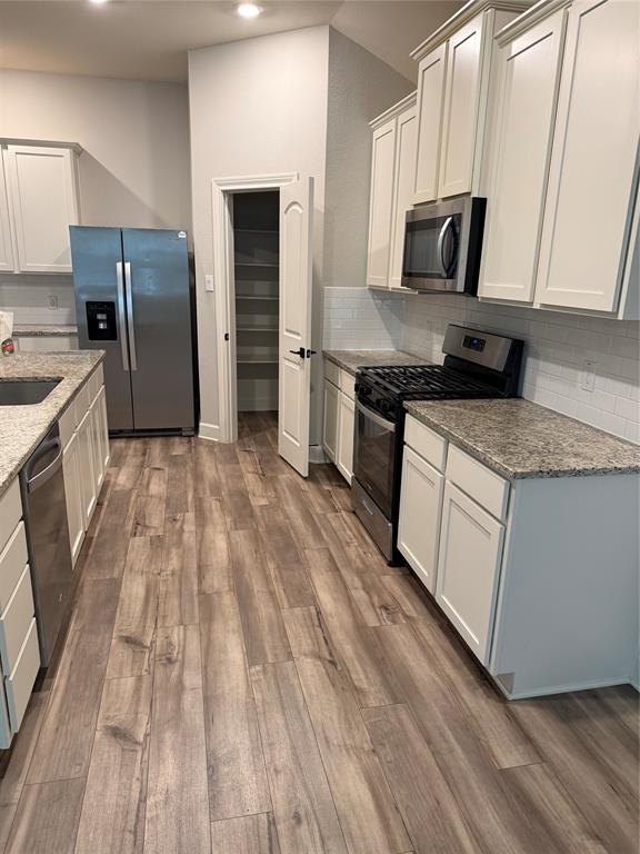 Kitchen with wood-finish flooring, white cabinetry, integrated stainless steel appliances, speckled countertops, and a subway tile backsplash