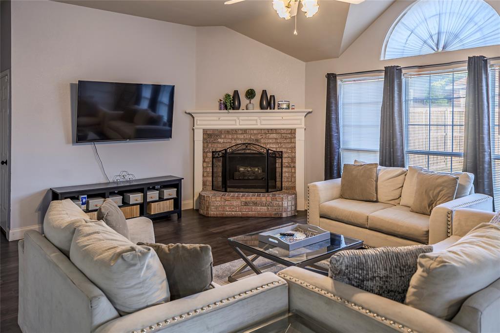 Vaulted ceiling, brick fireplace with mantel, dark wood-finish flooring, large arched window, and ceiling fan with light fixture Vaulted ceiling, brick fireplace with mantel, dark wood-finish flooring, large arched window, and ceiling fan with light fixture