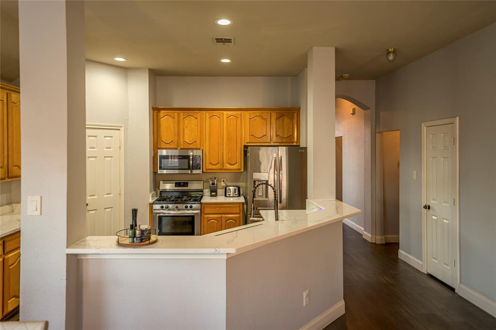Kitchen featuring wood cabinetry, stainless steel appliances, and a breakfast bar with a light-toned countertop Kitchen featuring wood cabinetry, stainless steel appliances, and a breakfast bar with a light-toned countertop