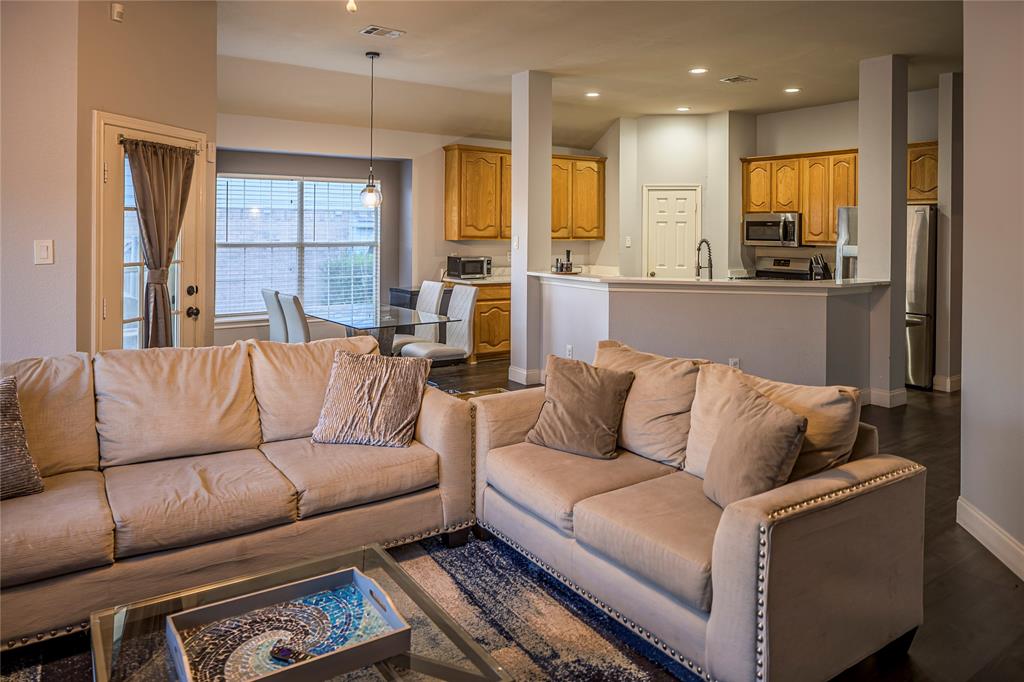 Open-concept living area featuring dark wood-finish flooring, recessed lighting, and a kitchen with wood cabinetry and stainless steel appliances Open-concept living area featuring dark wood-finish flooring, recessed lighting, and a kitchen with wood cabinetry and stainless steel appliances