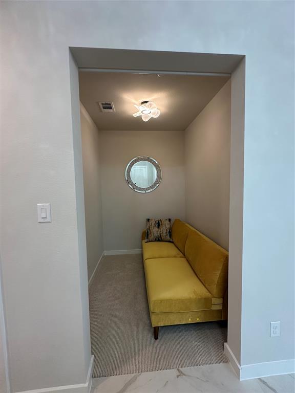 Carpeted alcove featuring a decorative ceiling light fixture and a circular wall mirror
