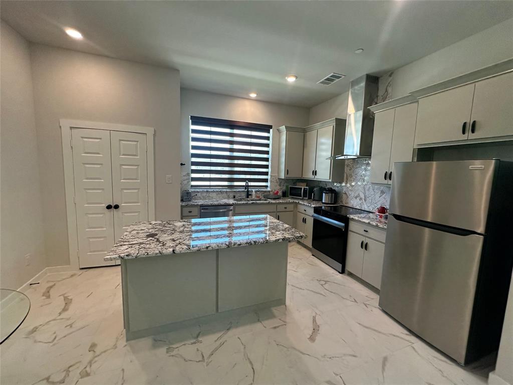 Modern kitchen featuring stainless steel appliances, white cabinetry with hardware accents, and a large waterfall-edge island with patterned quartz countertops Modern kitchen featuring stainless steel appliances, white cabinetry with hardware accents, and a large waterfall-edge island with patterned quartz countertops