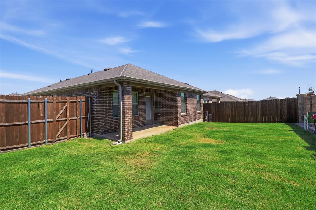 Expansive backyard featuring a manicured lawn, brick exterior, full wood privacy fence, and a covered patio