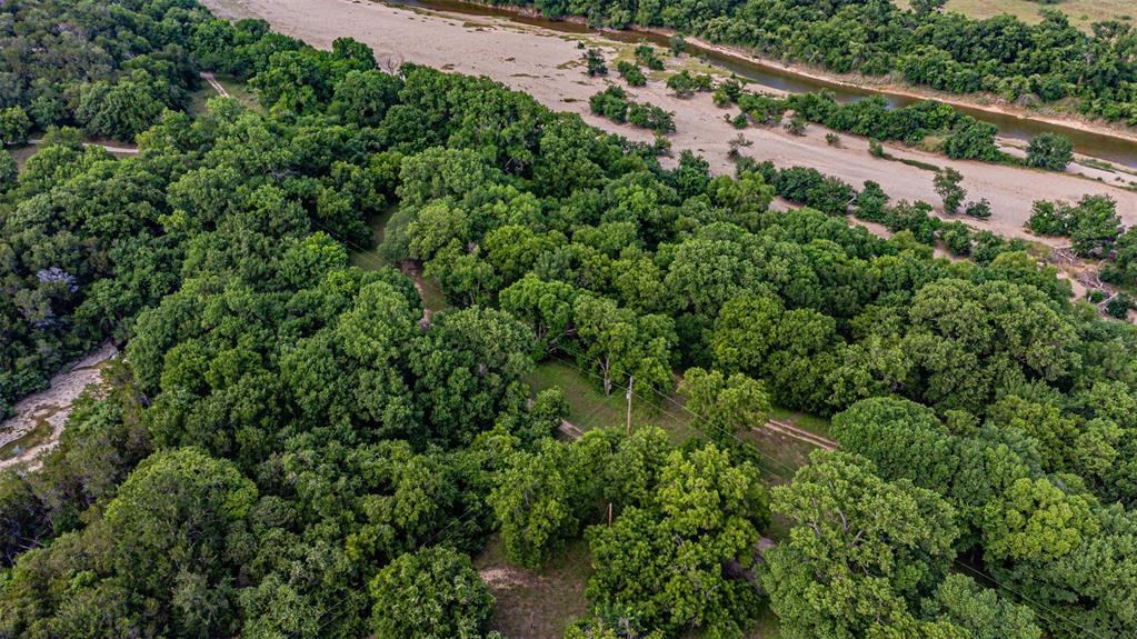 Expansive natural acreage featuring a dense tree canopy, a meandering river, and a light-colored riverbed