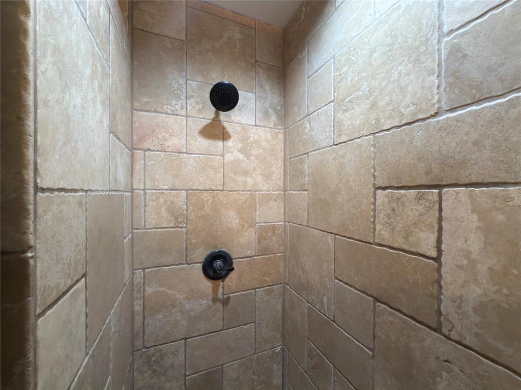 Shower enclosure with natural stone-look tile, dark bronze-finish shower head, and dark bronze-finish shower controls