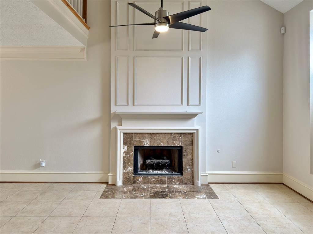 Two-story living area featuring a fireplace with stone tile surround, decorative mantel, and paneling, complemented by a ceiling fan and light-toned tile flooring