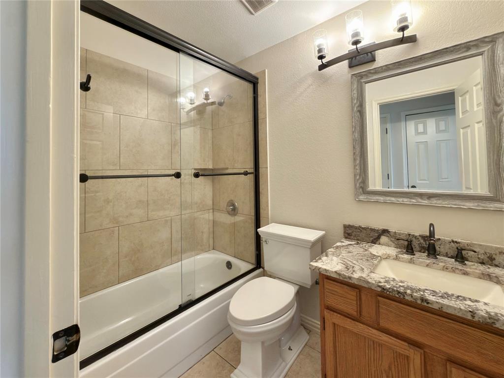 Spa-inspired ensuite bathroom featuring a frameless glass-enclosed shower with tile surround, soaking tub, dual-sink vanity with granite countertop, wood cabinetry, and brushed nickel fixtures