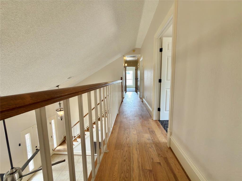 Wood-finish flooring throughout the hallway, white painted walls, and a white railing with a wood-finish handrail