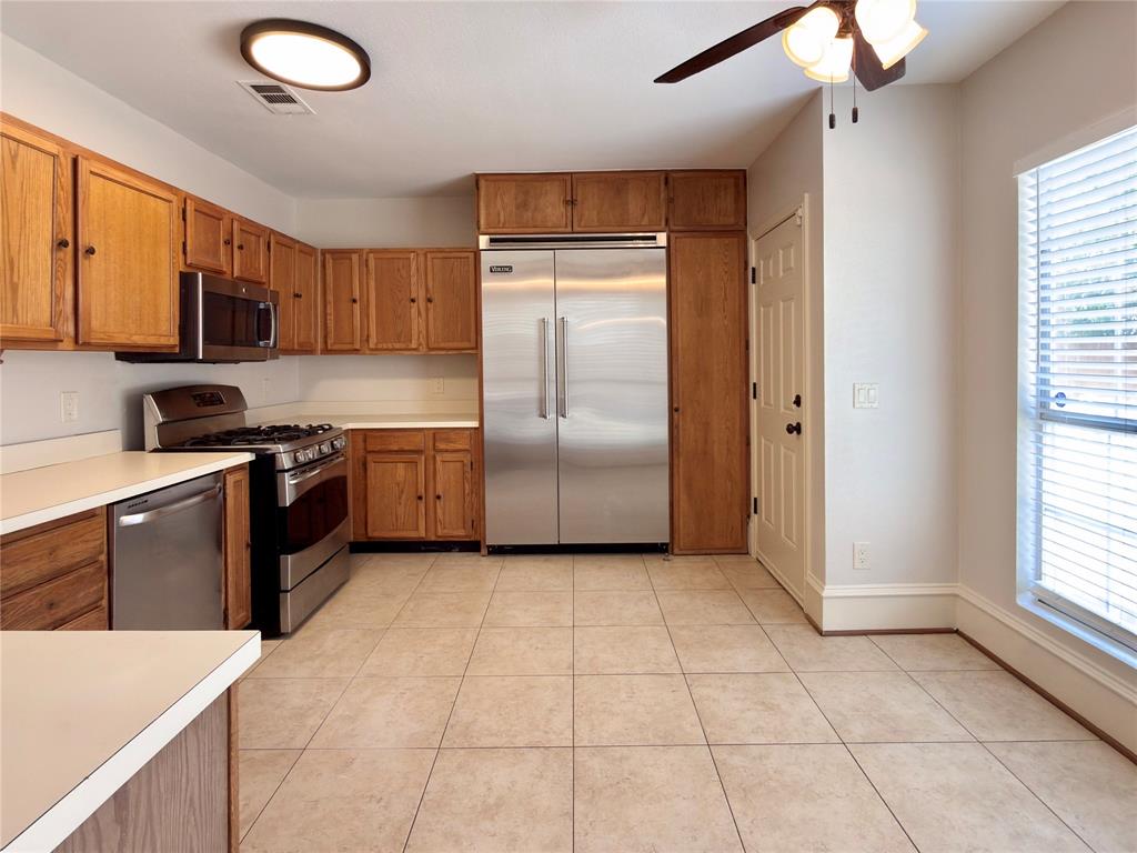 Kitchen featuring stainless steel appliances, wood cabinetry, light-toned countertops, tile flooring, and a ceiling fan