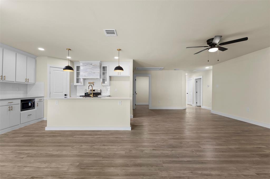 Kitchen featuring white shaker-style cabinetry, wood-finish flooring, a central island with a gold-toned faucet, pendant lighting, and a mounted ceiling fan