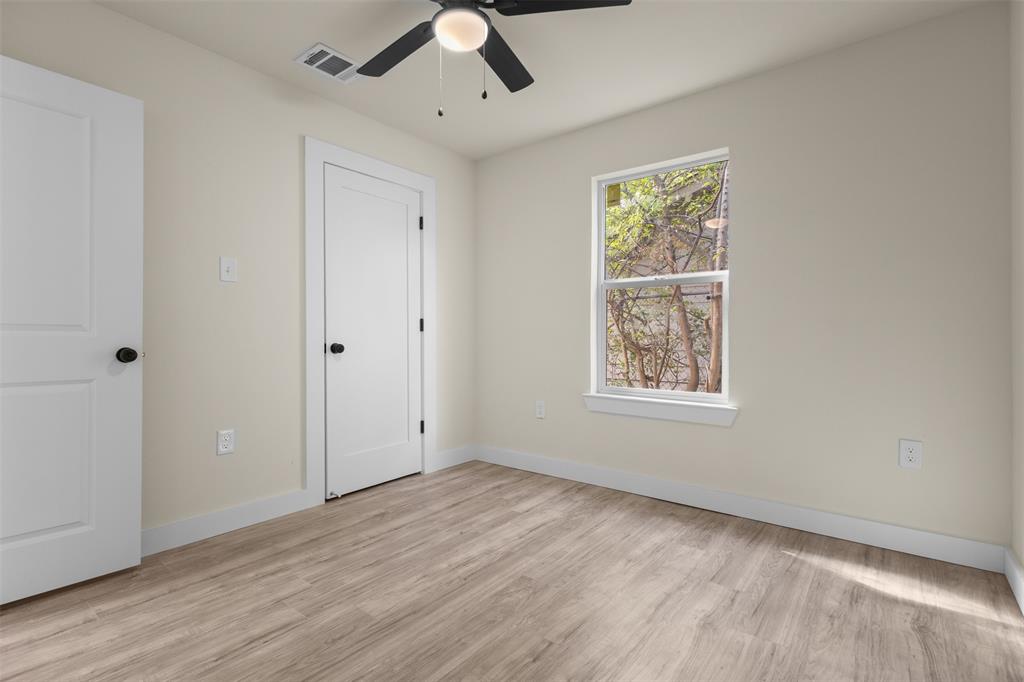 Neutral interior with wood-finish flooring, white panel doors with matte black hardware, and a ceiling-mounted light fixture with a fan