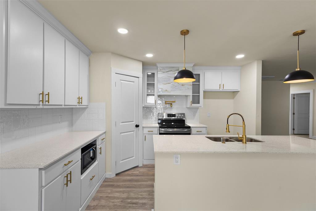 Kitchen featuring white shaker-style cabinetry with gold-tone hardware, quartz countertops, a central island with a gold-finish faucet, recessed lighting, and dual matte black pendant lights