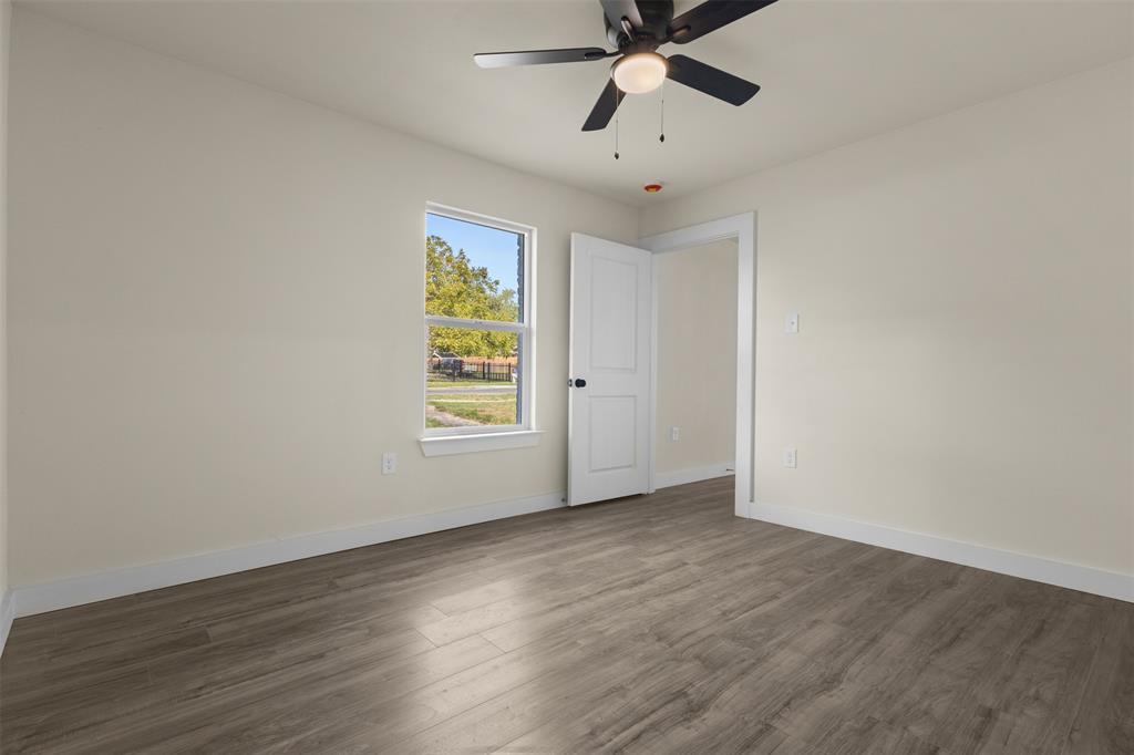Room featuring wood-finish flooring, a multi-blade ceiling fan with integrated lighting, and a single-pane window with white trim