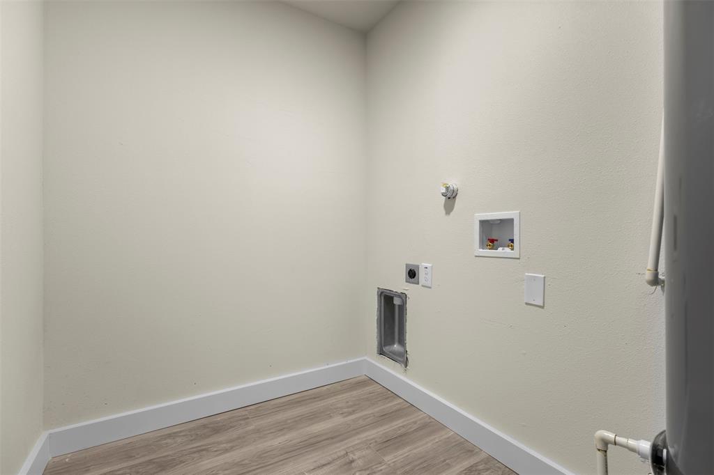 Dedicated space featuring wood-finish flooring, wall-mounted utility connections, and integrated plumbing access panels