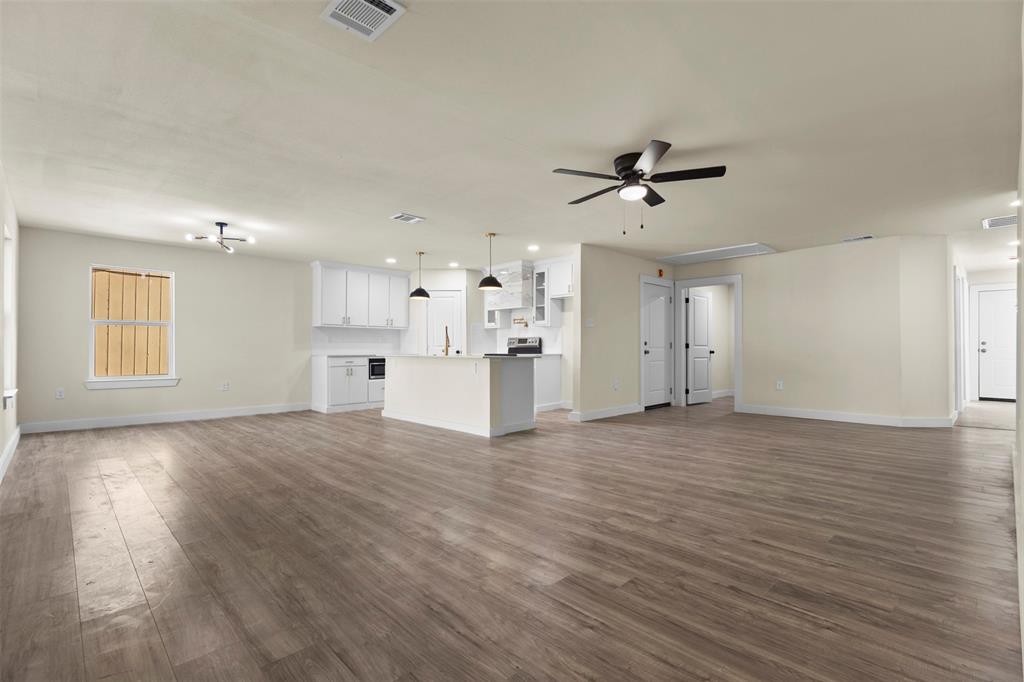 Open-concept interior featuring wood-finish flooring, white cabinetry, a center island with a stone-finish countertop, pendant lighting, and ceiling fans