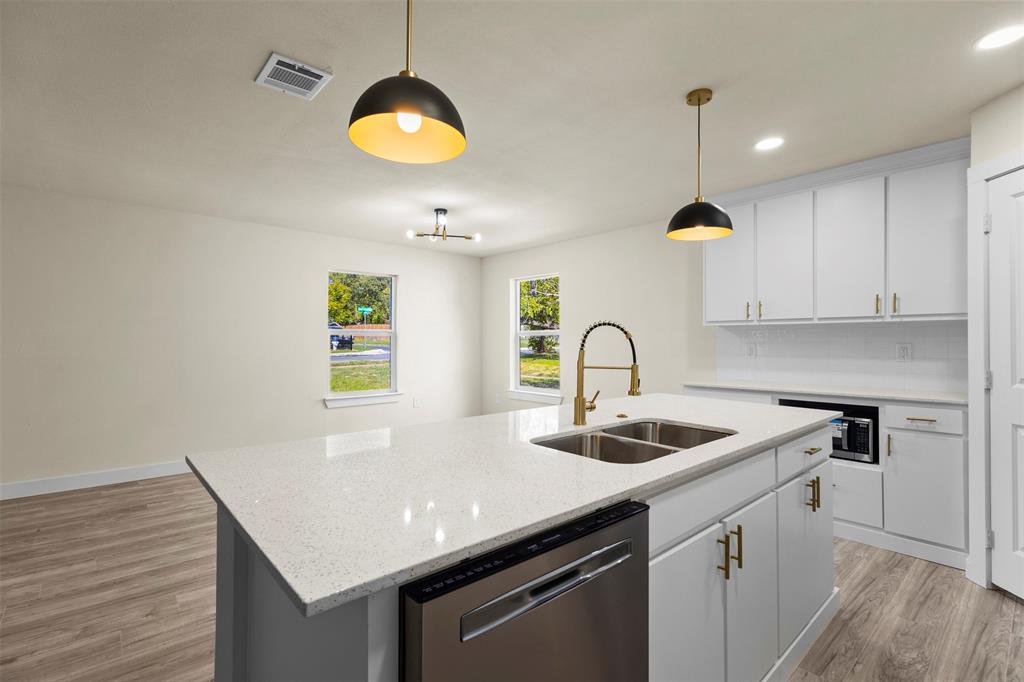 Kitchen featuring a central island with a solid surface countertop, double-basin undermount sink, brass-finish gooseneck faucet, white cabinetry with brass-finish hardware, and wood-finish flooring